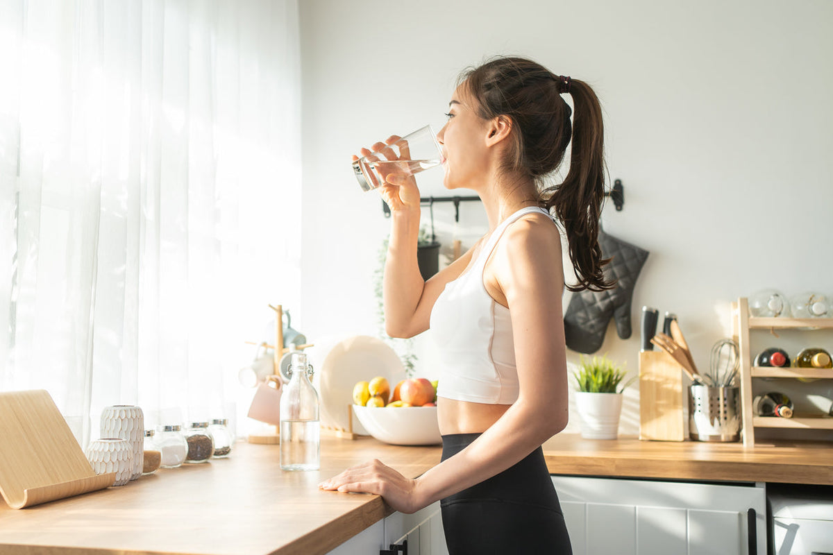 femme qui boit de l'eau dans sa cuisine en tenue de sport  Image